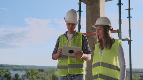 Professional-engineers-in-safety-vests-and-helmets-working-with-digital-tablet-and-blueprints